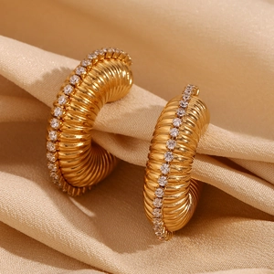 Detail of gold hollow C-shape earrings with textured ribs and cubic zirconia inlay