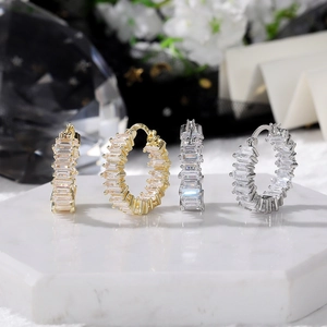 Close-up of gold and silver baguette-cut CZ hoop earrings on white marble display tray