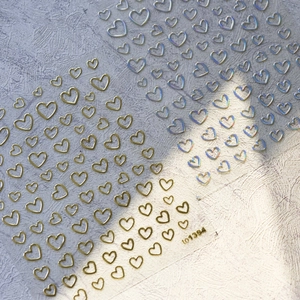 Pegatinas 3D para uñas con corazones dorados y plateados sobre un fondo púrpura