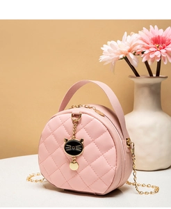 Pink quilted round crossbody bag with cute cat charm and gold chain strap in aesthetic setting
