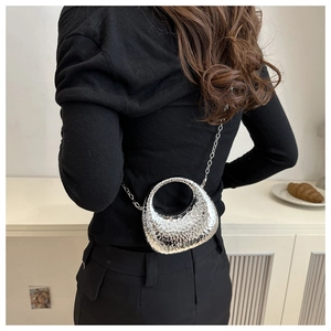 Sac bandoulière rond argenté avec texture martelée et chaîne en métal porté par modèle