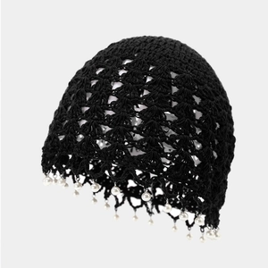 Detail of black crochet beanie featuring delicate hollow patterns and white pearl charms