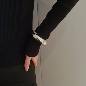 Polished chunky silver bangle bracelet worn over a black sweater sleeve for style