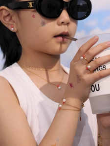 Detalle de set de joyería infantil con perlas y flores rojas en collar y pulsera dorados