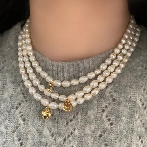 Close-up of triple-layered freshwater pearl necklace with gold heart and smiley pendants