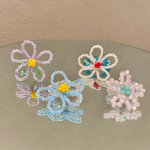 Détail de quatre bagues de fleurs en perles faites main sur une surface miroir réfléchissante