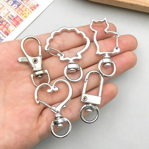 Silver metal lobster clasps and cute shaped keychains held in hand for DIY jewelry