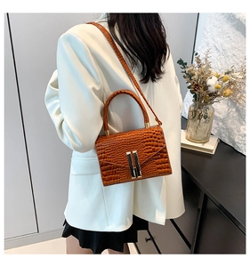Detailed view of crocodile embossed leather texture and gold buckle on brown handbag