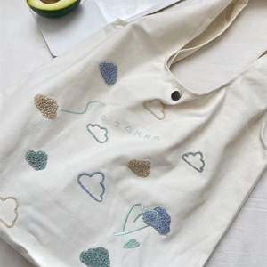 Top view of cream canvas tote bag featuring cloud embroidery and metallic snap button
