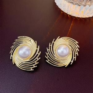 Detailed view of gold spiral metal earrings with pearls on dark brown leather texture