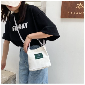 Outdoor shot of a white canvas bucket bag with vintage green label and shoulder strap
