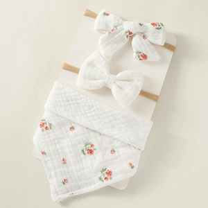 Close-up of floral muslin baby bib and matching bow headbands on display card