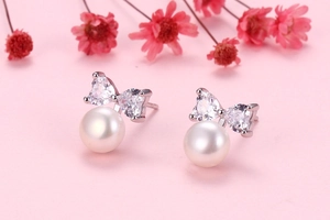 Macro shot of silver bow pearl earrings with zircon stones on soft pink background
