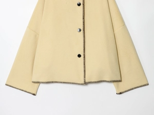 Detail of light yellow coat featuring black buttons and contrast blanket stitching finish