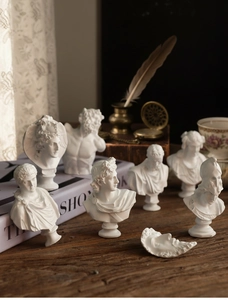 Classical mini resin busts on a vintage wooden desk with old books and a quill pen