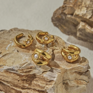 Dettaglio di quattro ear cuff dorati con perle su una superficie di roccia naturale