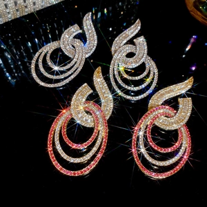Macro detail of geometric hollow drop earrings featuring nested ovals and pink pavé crystals