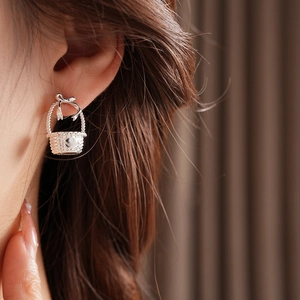 Close-up of silver bow basket earring with a delicate pearl bead on soft fabric