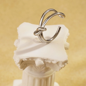 Elegante anello a doppio nodo argento su piedistallo bianco con sfondo caldo e minimale