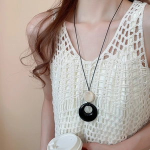 Detail einer Boho-Kordelkette mit beigem Harzanhänger und schwarzem ausgeschnittenem Ring