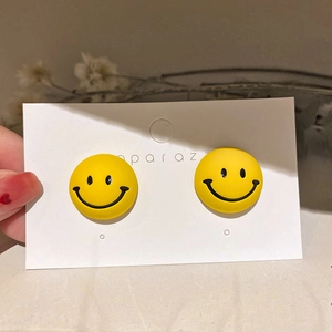Detailed close-up of yellow smiley face stud earrings on a white display card