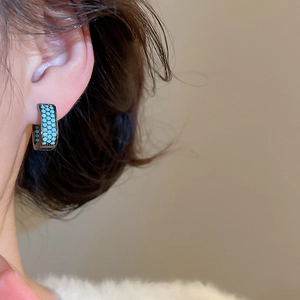 Close-up of turquoise square hoop earring with black metal frame on model ear