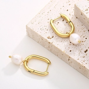 Detail of gold U-shaped hollow earrings with hanging round white pearls on stone