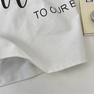 Close-up of minimalist white canvas tote bag with black TO OUR B typography and texture