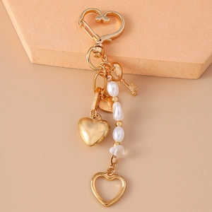 Close-up of golden keychain with heart pendant, pearls, and a small key charm on beige stone