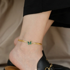 18K gold plated anklet with green butterfly pendant worn on ankle over soft beige fabric