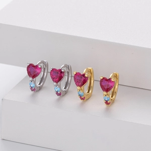Detailed view of silver and gold heart ruby earrings on a white geometric display stand