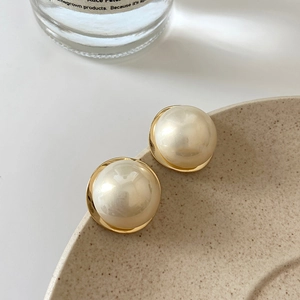 Detail of round pearl stud earrings with gold base on a minimalist ceramic plate