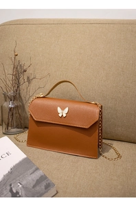 Detail of a brown leather crossbody bag with butterfly clasp on a soft fabric sofa