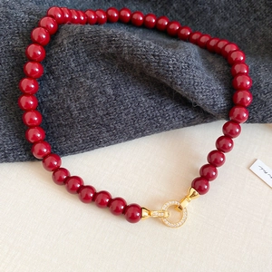 Macro shot of dark red beaded necklace featuring a gold buckle with micro-inlaid zircons