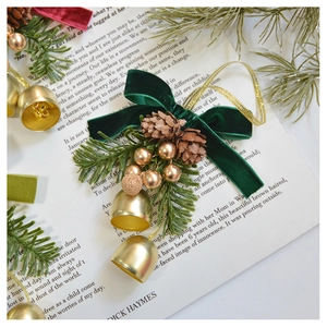 Close-up of velvet bow Christmas ornament with gold bells and pine cone on vintage book