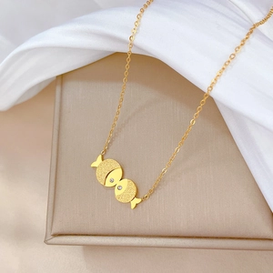 Close-up of golden kissing fish pendant with small crystals on white silk background