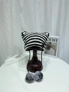 Detail of knit cat ear hat with black stripes and soft grey fluffy pom-poms on a stand