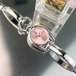Close-up of a vintage silver watch with pink dial and chain strap on reflective surface