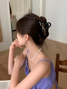 Rear view of a model wearing a large silver metal bow hair claw clip with black accents