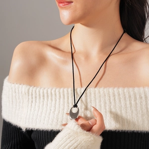 Detail of silver oval hollow pendant on black cord worn by a model against a grey background