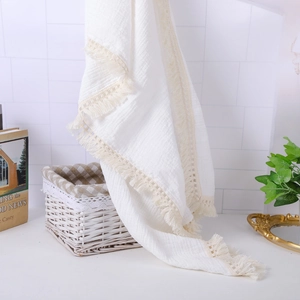 Detail of white muslin cotton baby blanket with beige lace tassel trim on a wicker basket