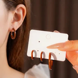 Fashionable brown C-shaped resin hoop earrings with glossy finish shown on model and card