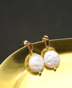 Macro shot of gold drop earrings with emerald cut red stones and baroque pearls