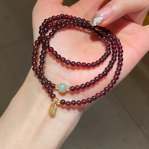 Close-up of garnet beads with a green jade bead and golden fortune charm on a bracelet