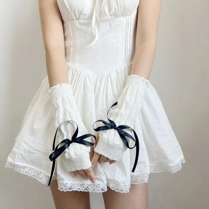 Detail of white cable knit arm warmers featuring delicate black ribbon bow accents