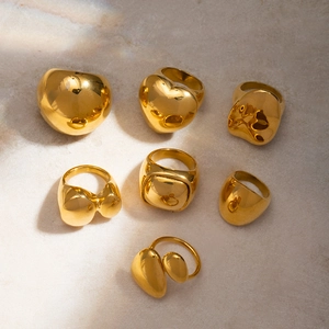 Polished 18k gold chunky oval and heart rings on beige marble with sunlight