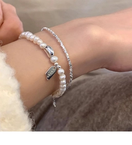 Detail of layered S925 silver lucky charm bracelet with fresh water pearls on a wrist