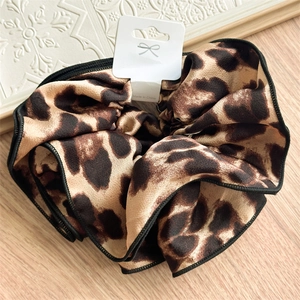 Close-up of leopard print satin scrunchie with black edging on a wooden surface