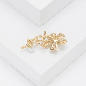 Detailed back view of gold flower brooch showing pin clasp and pearl setting on white base
