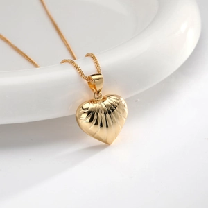 Detail of a golden heart pendant necklace with textured radial pattern on white ceramic